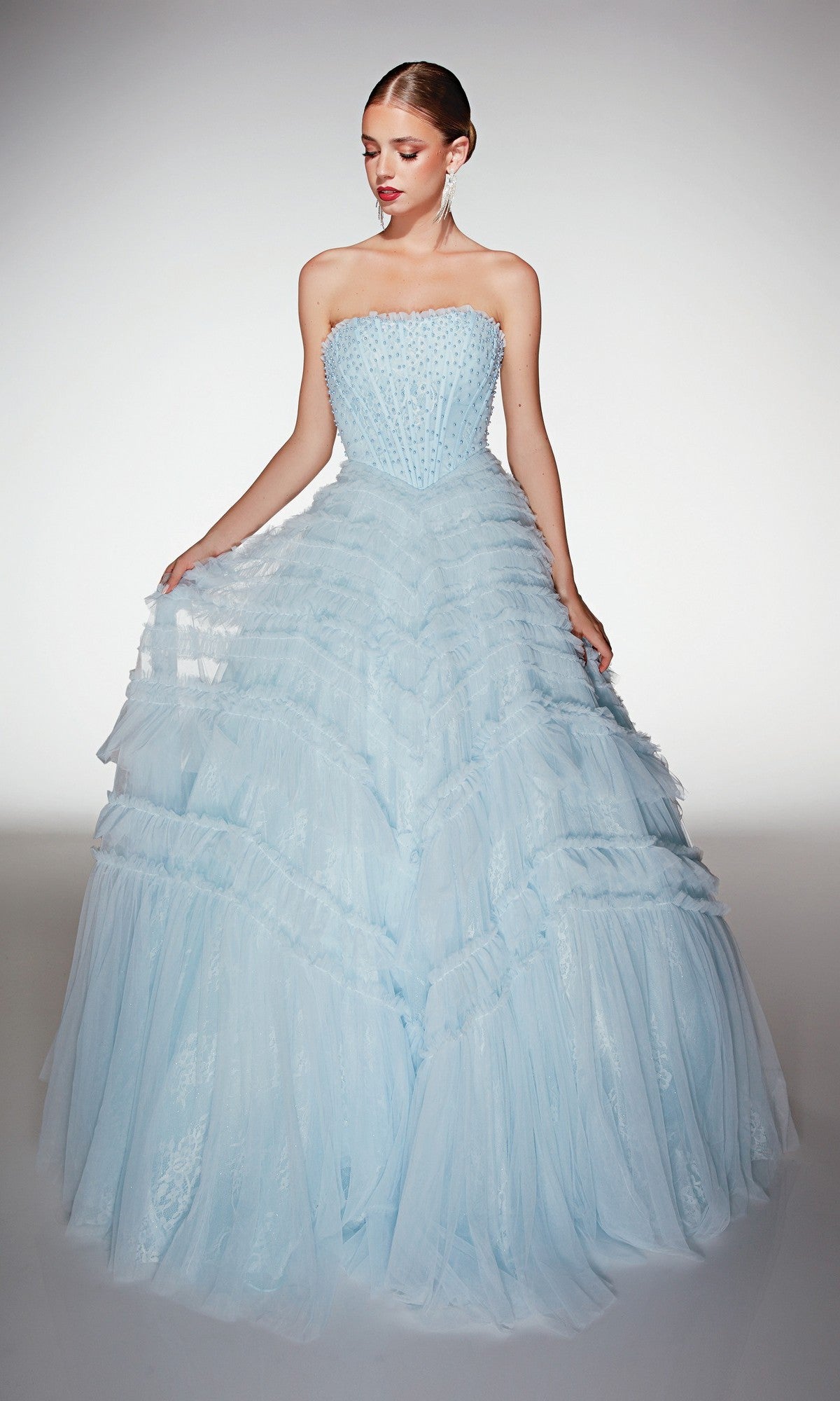 A woman stands in a studio wearing the Alyce 62208 long prom dress in sky blue, featuring a strapless fitted bodice with beaded details and a dramatic tulle ruffle ballgown skirt.